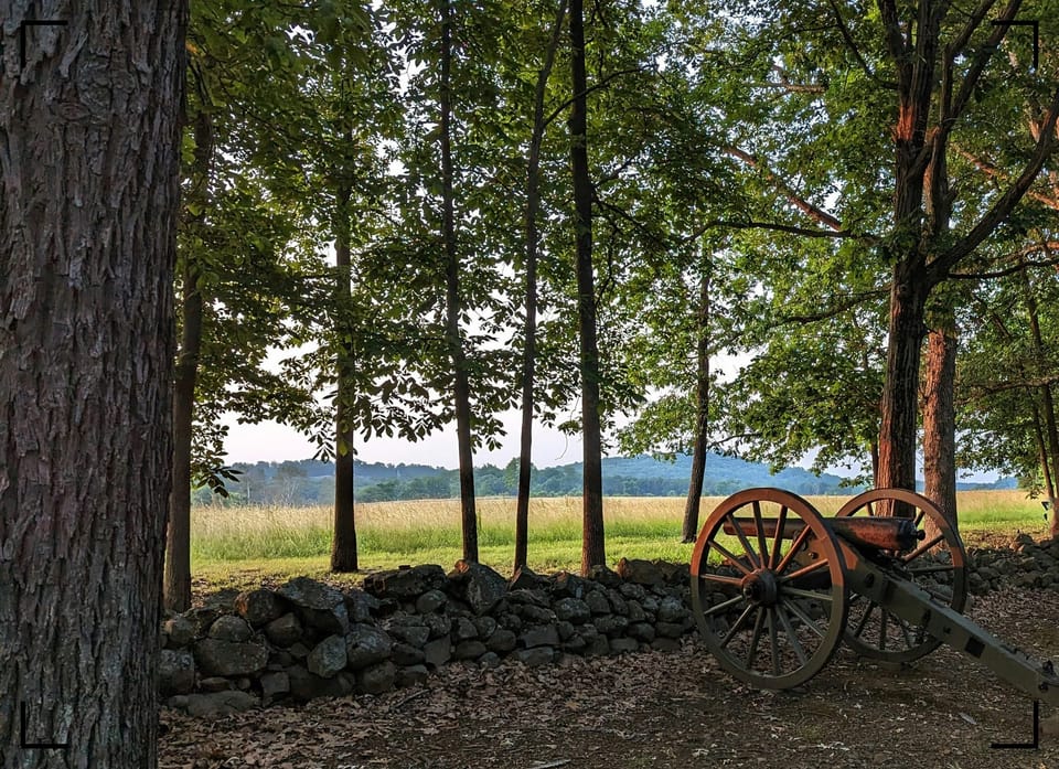 A quiet scene with a cannon behind a crumbling stone wall at the edge of the woods in Gettysburg National Military Park.